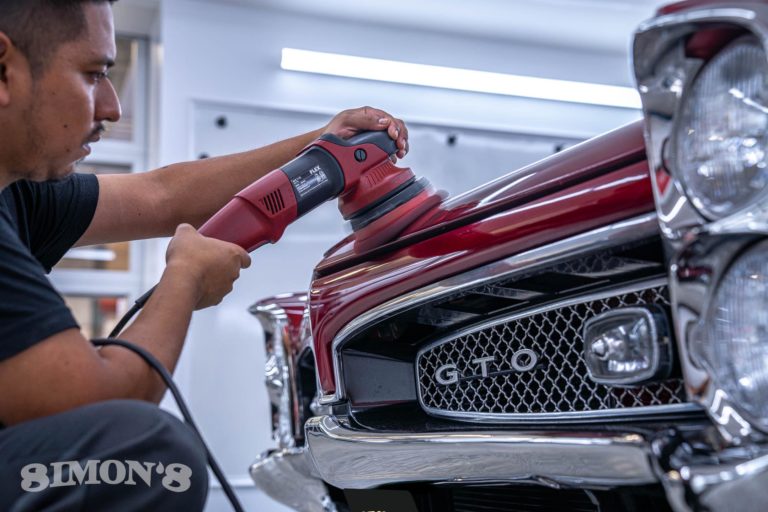 Detailer polishing the hood of a 1967 Candy Apple Red Pontiac GTO.