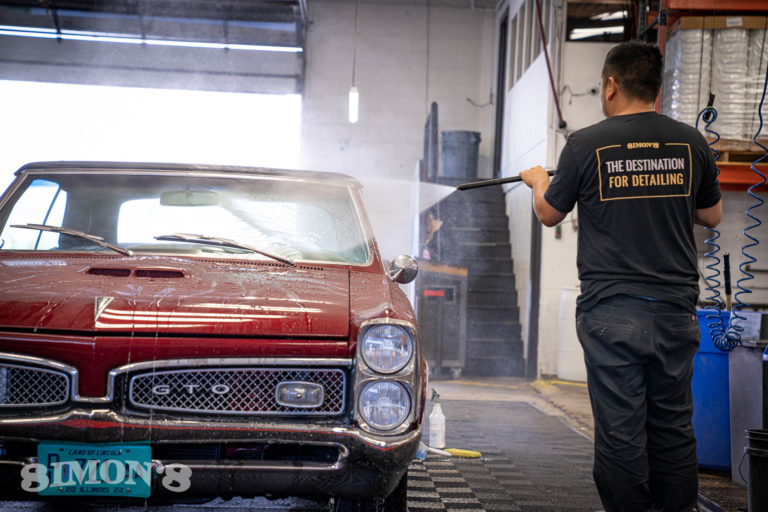 Pressure washing the windshield of a 1967 Candy Apple Red Pontiac GTO.