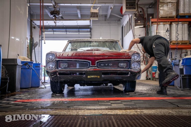 Detailer washing a 1967 Candy Apple Red Pontiac GTO from a front-on view.